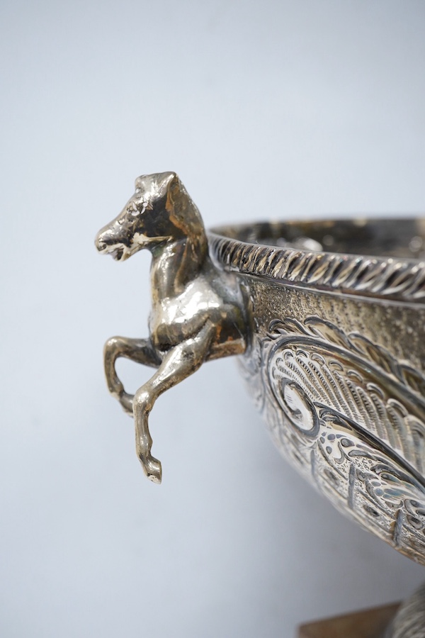 A 20th century continental white metal two handled pedestal bowl, stamped '900 SK', with horses head handles and embossed with a suspension bridge amid scrolls, diameter 28.6cm, 45.4oz, with a wooden plinth. Condition -